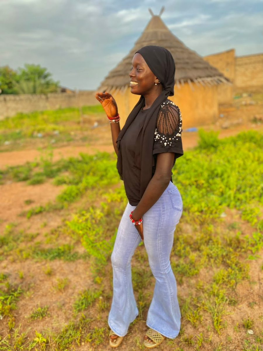 Rima in profile in front of a thatched hut